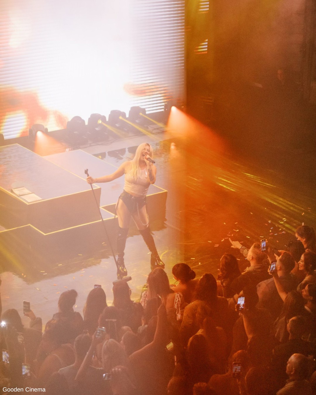 Kesha sings to a crowd on stage in thigh high black boots.