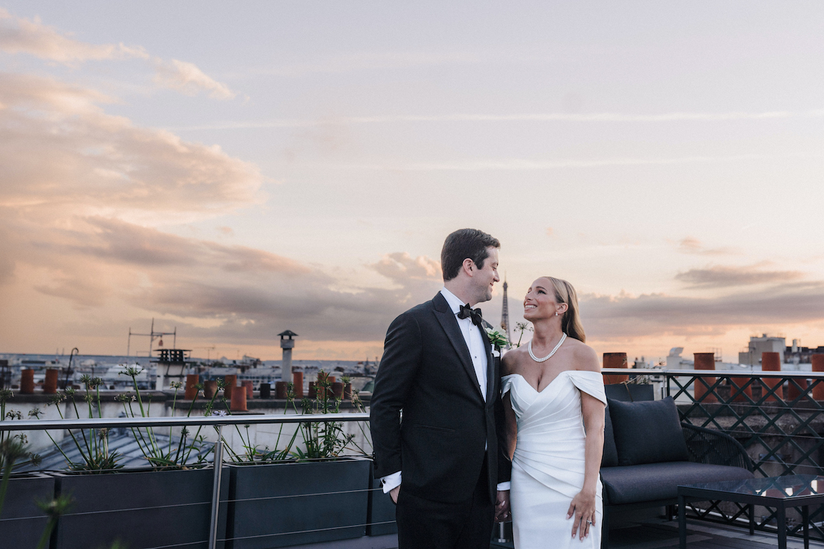 bride and groom smile at each other as the sunsets on Paris and the Eiffel Tower in the back