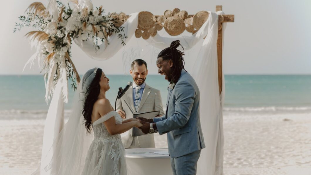 bride and groom smile at each other at the floral altar of their beach wedding