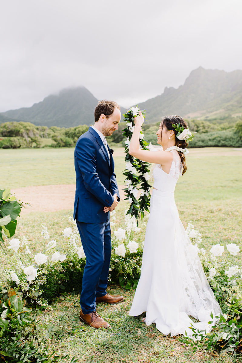 bride places Hawaiian lei over groom's shoulders