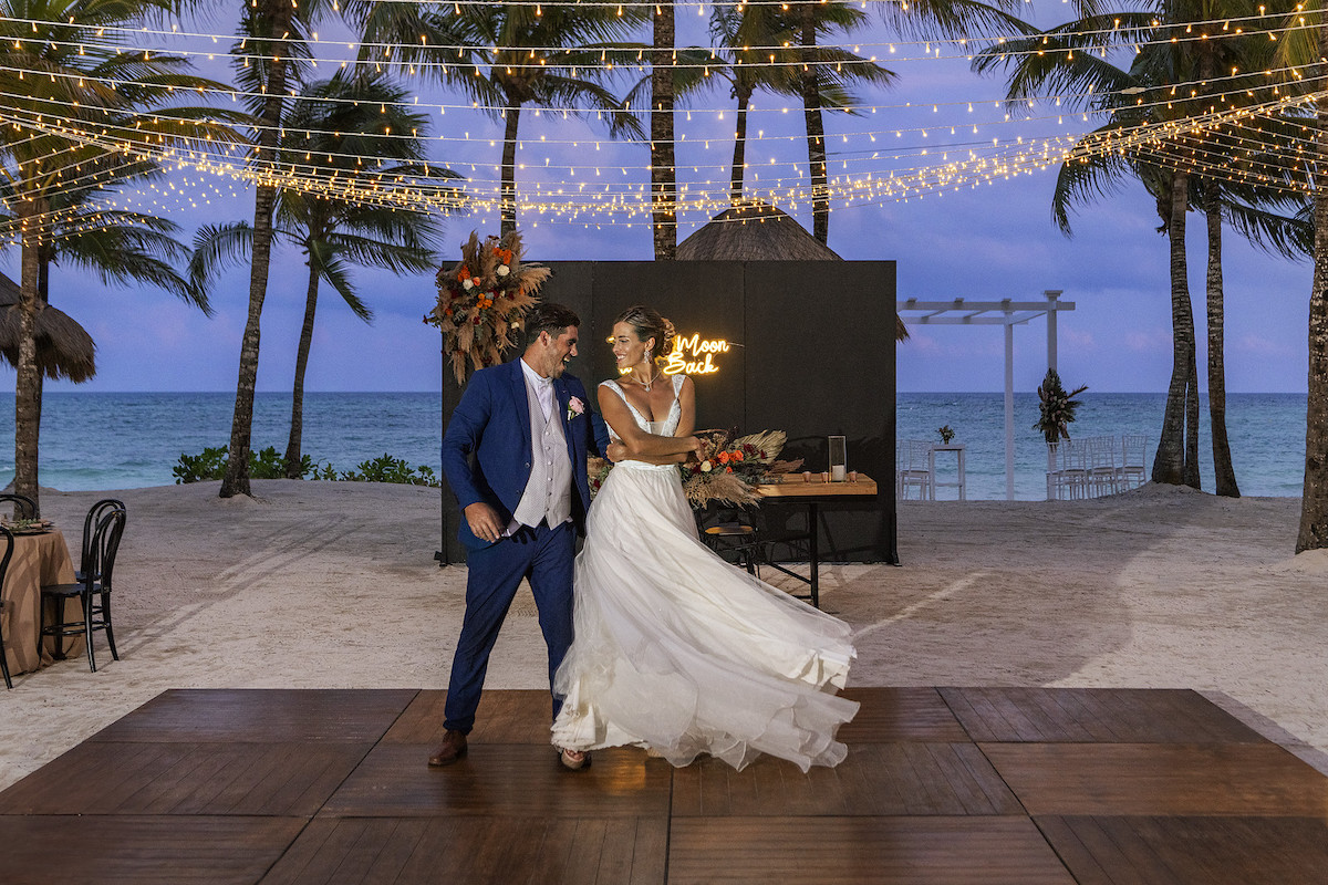 groom spins his bride on a dance floor laid over sand