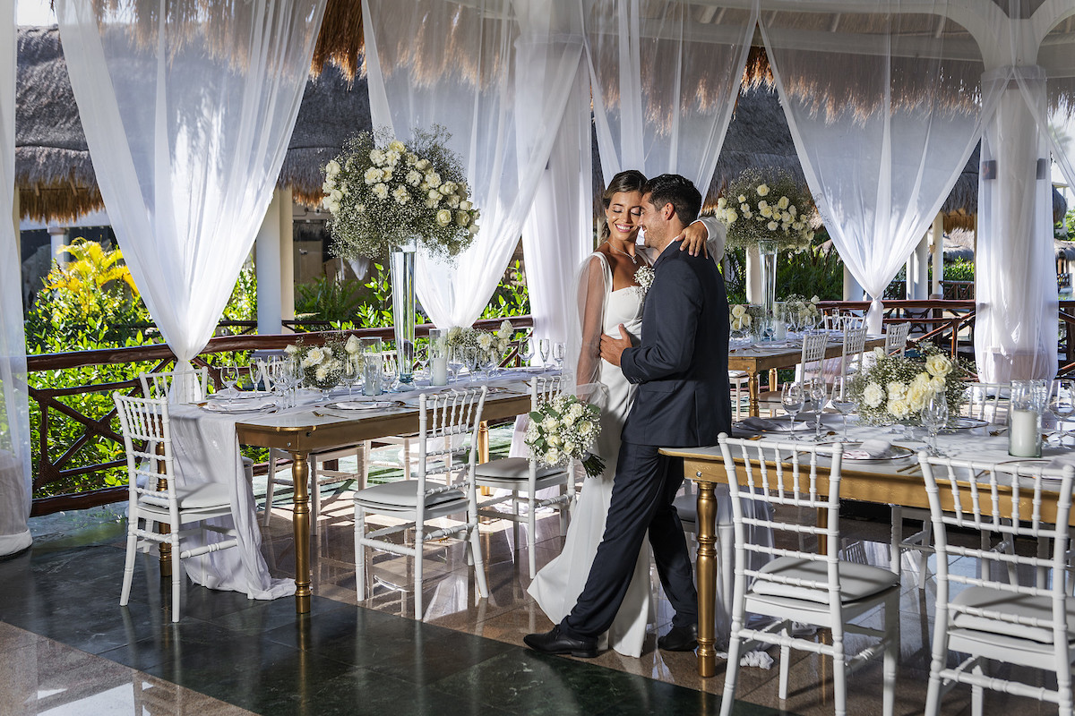 bride and groom embrace surrounded by a reception setup with baby's breath florals and white roses