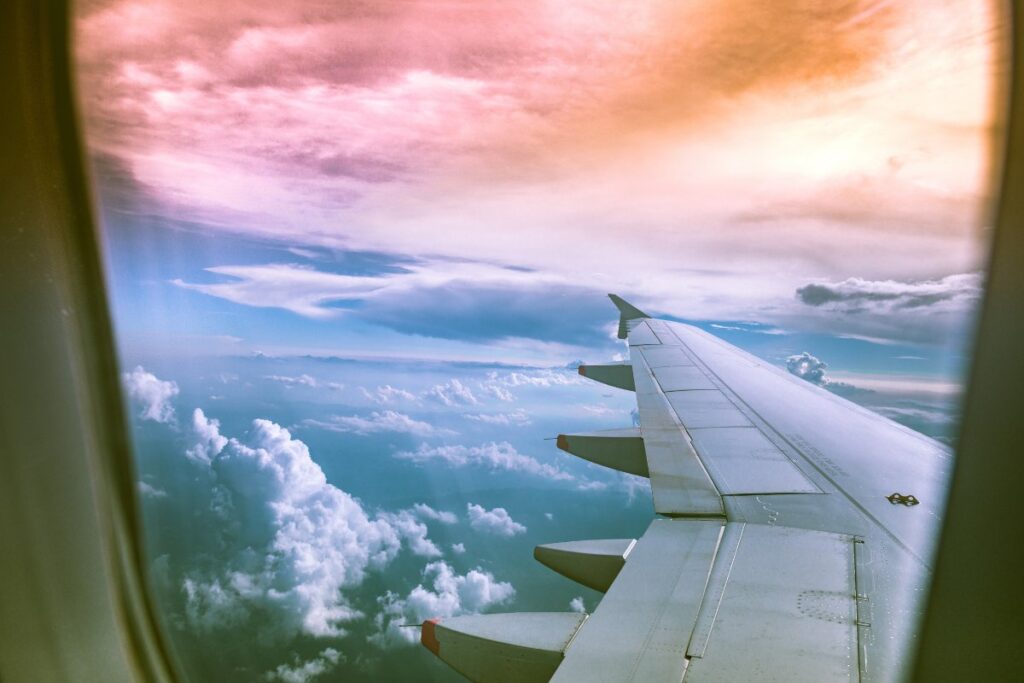 View from an airplane window showing the wing and a scenic sky with clouds and a colorful sunset.