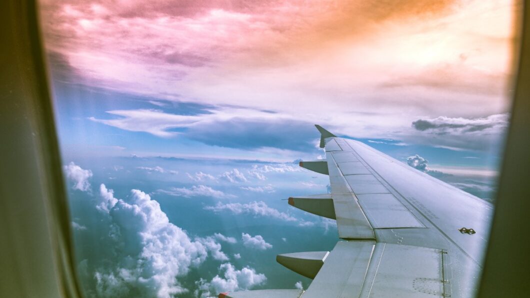 View from an airplane window showing the wing and a scenic sky with clouds and a colorful sunset.