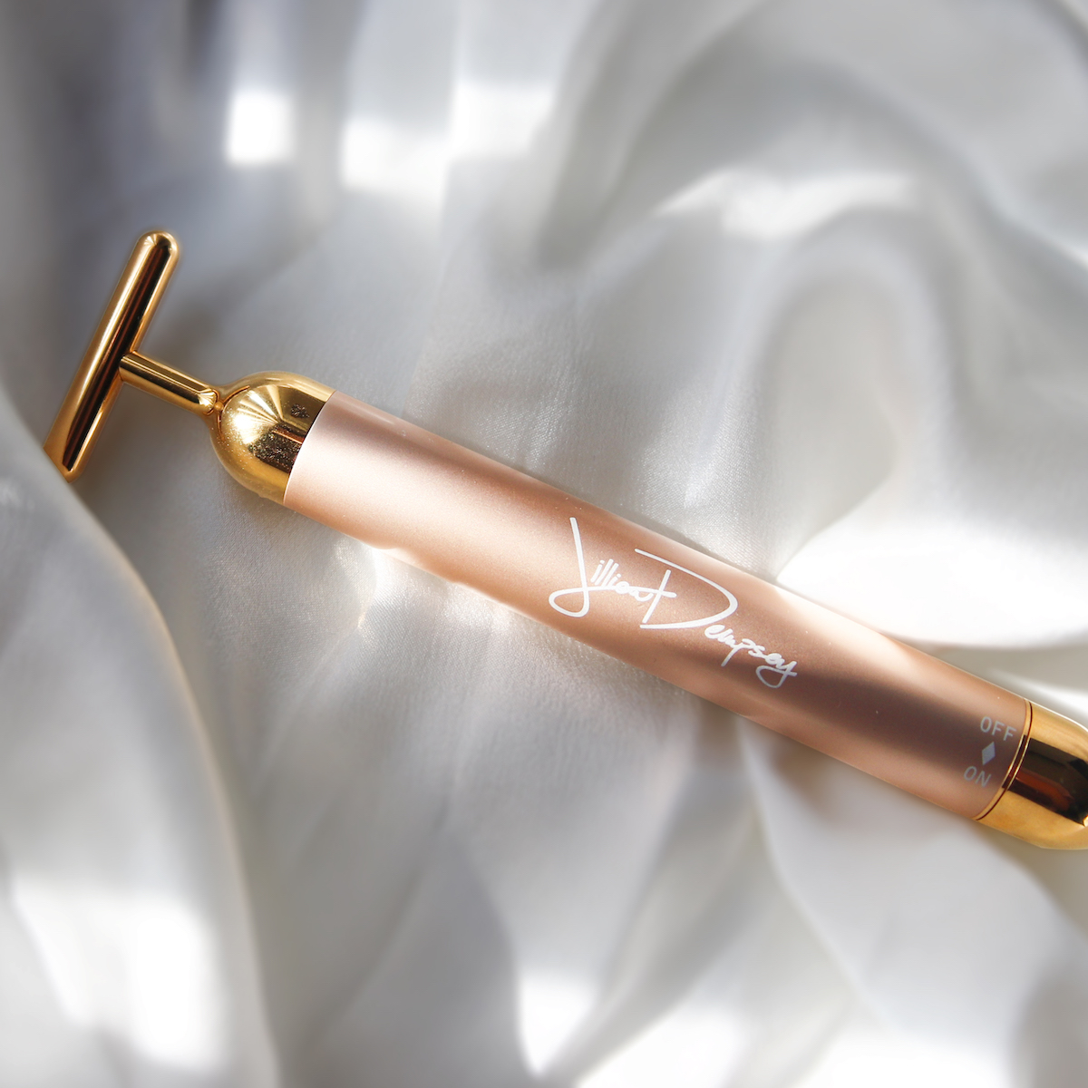 Gold and beige skincare device with a T-shaped head and text "Jillian Dempsey" on the handle, placed on white fabric.