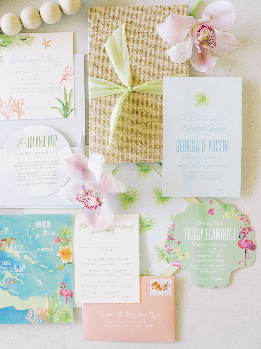 A collection of colorful and tropical-themed wedding invitations and RSVP cards, decorated with pink orchids and a gift-wrapped item in the center.