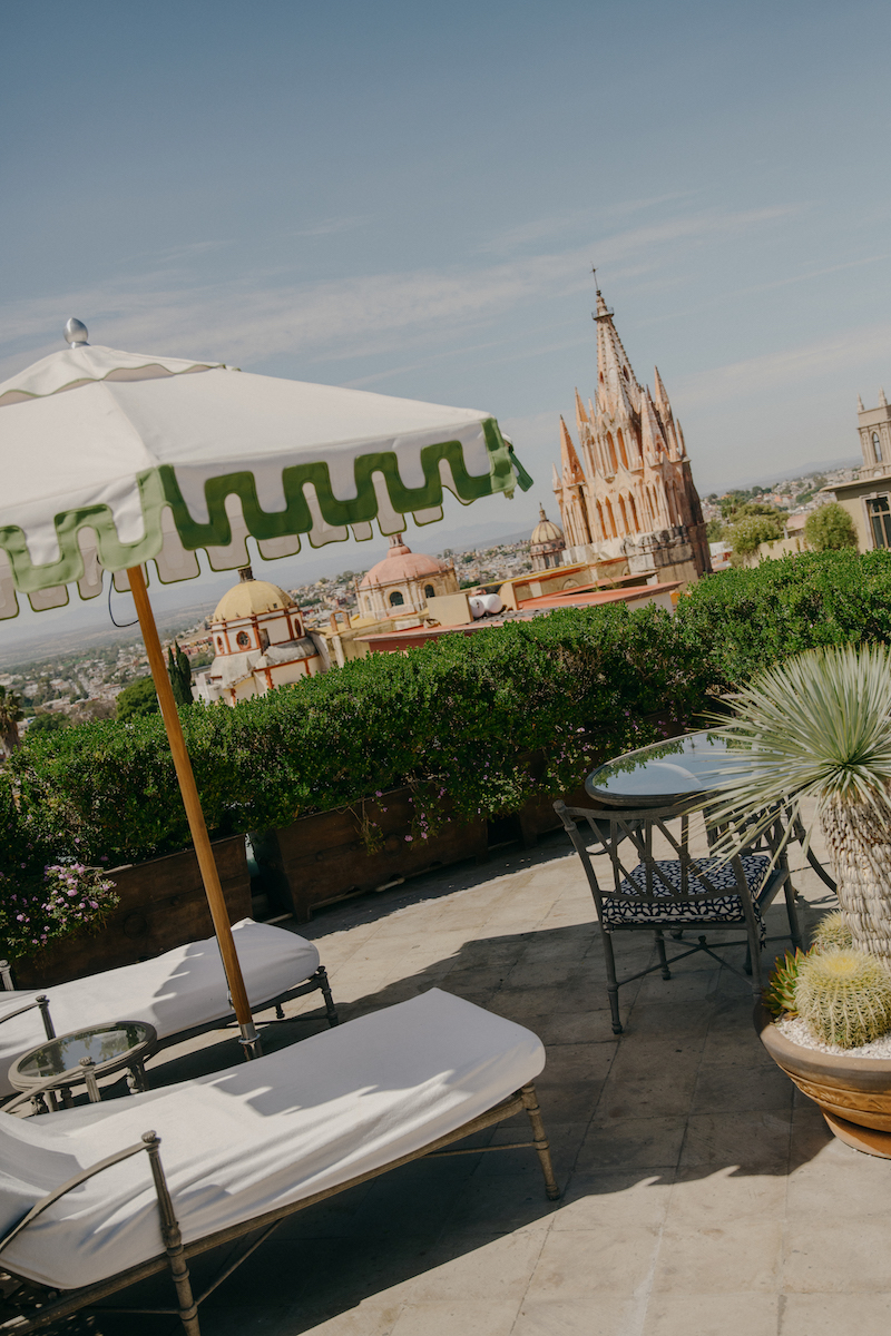 Rooftop patio with lounge chairs and umbrella, overlooking the Parroquia de San Miguel Arcángel and cityscape in San Miguel de Allende, Mexico.