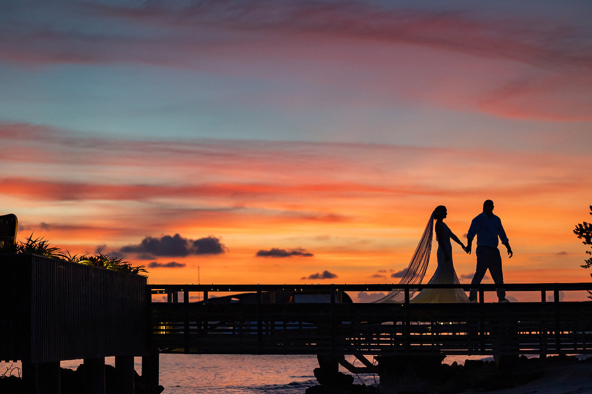 Silhouetted couple walking on a bridge during a colorful sunset.