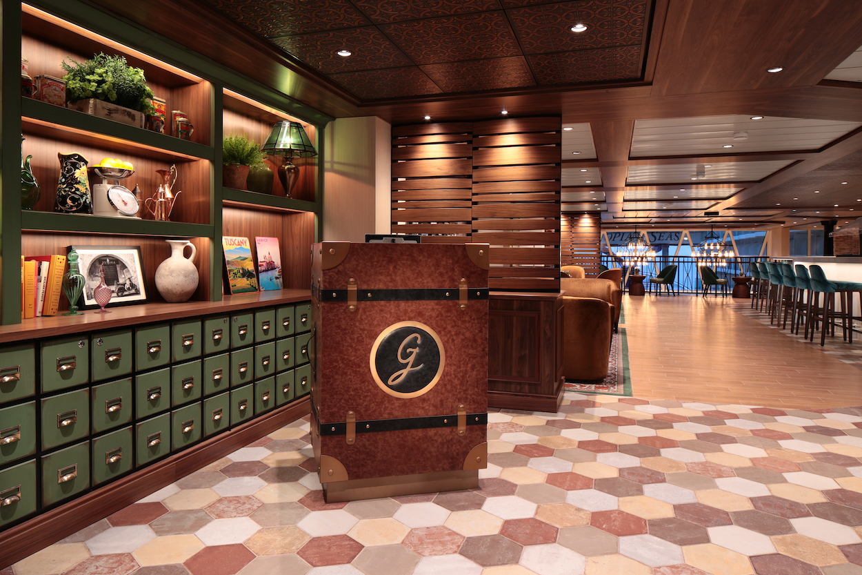 Lobby area with wooden decor, a reception desk with a "G" emblem, hexagonal tiled floor, bookshelves, and seating area in the background.