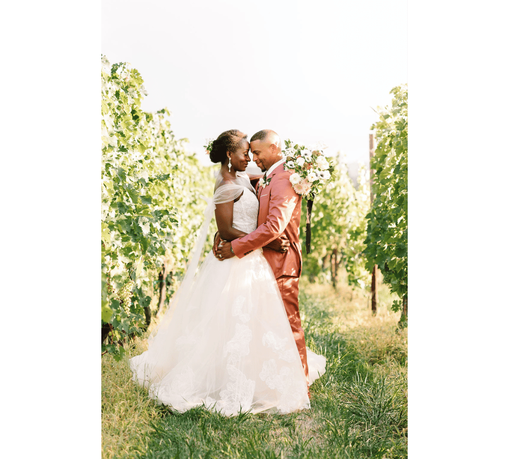 A bride and groom embrace in a vineyard.