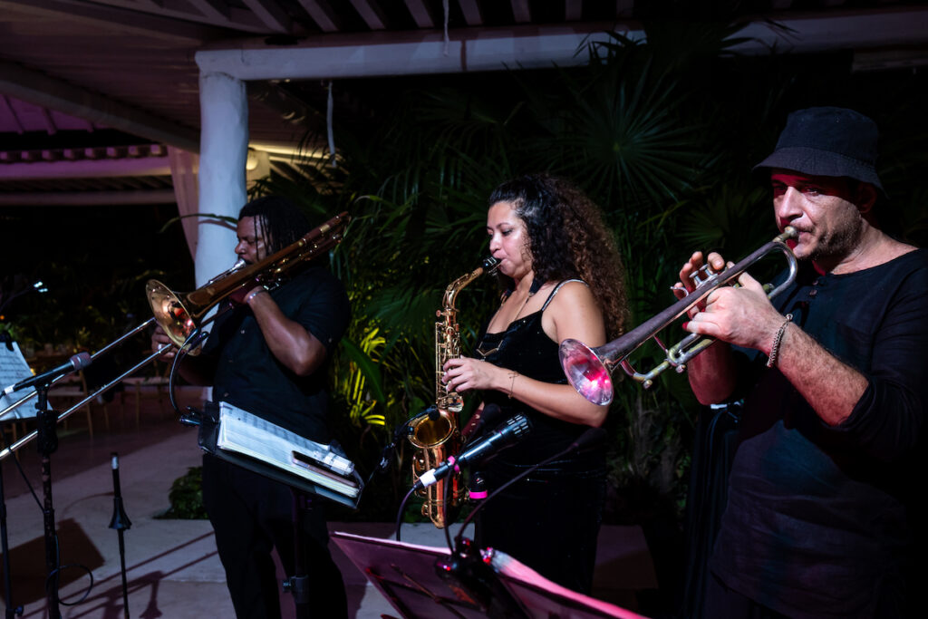 Three musicians perform on brass instruments outdoors at night.