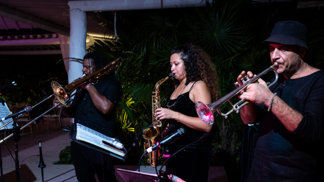 Three musicians perform on brass instruments outdoors at night.