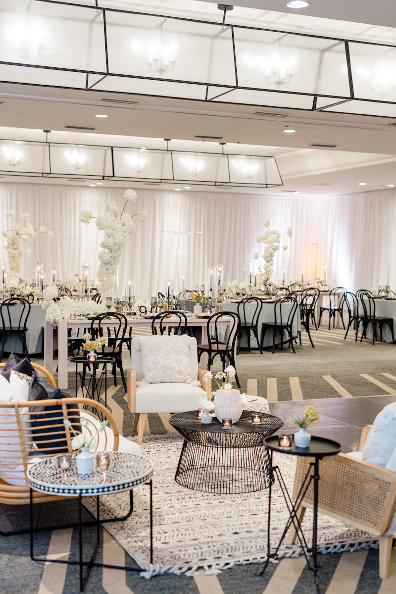 Elegant event space with white drapes, round tables with black chairs, and modern lounge area featuring cushioned seating and decorative elements.