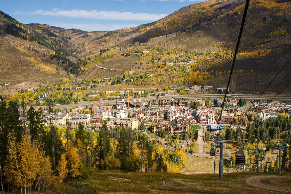 View of a town in a mountainous area during autumn, with colorful foliage and a cable car system running through the landscape.