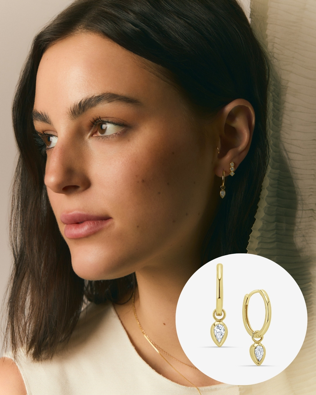 A woman wearing gold hoop earrings with a teardrop-shaped gem. There is an inset showing a close-up of the earrings.