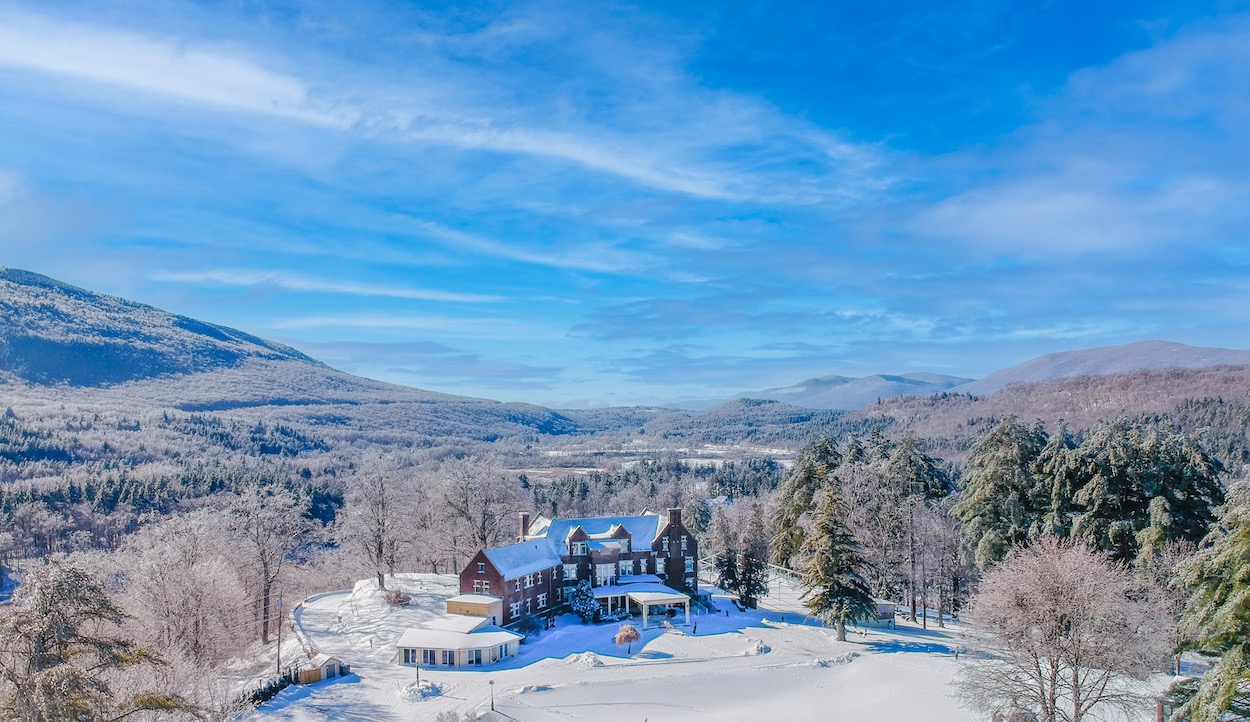 A large building surrounded by snow-covered trees and hills under a blue sky in a winter landscape.