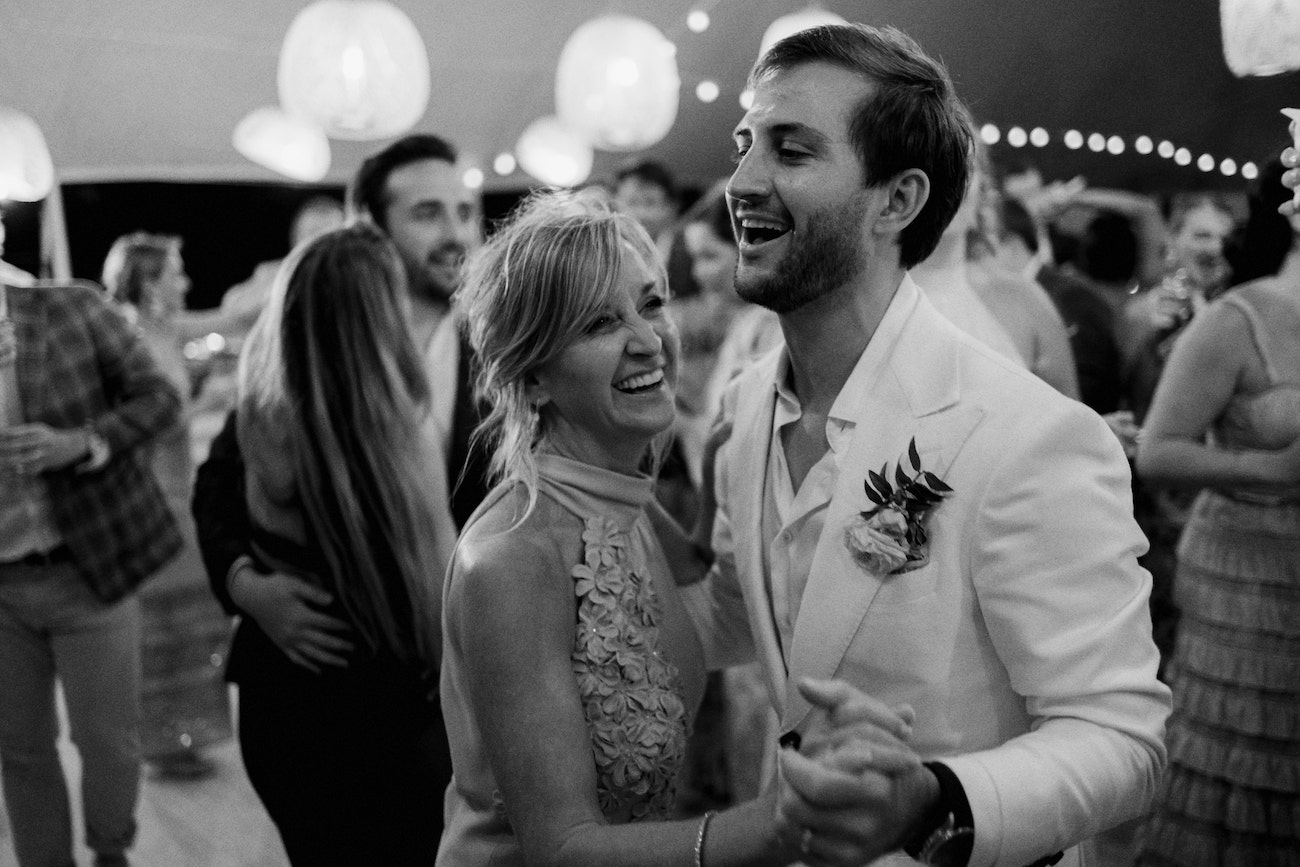 A woman and a man in formal attire smile and dance together at an indoor event with other people in the background.