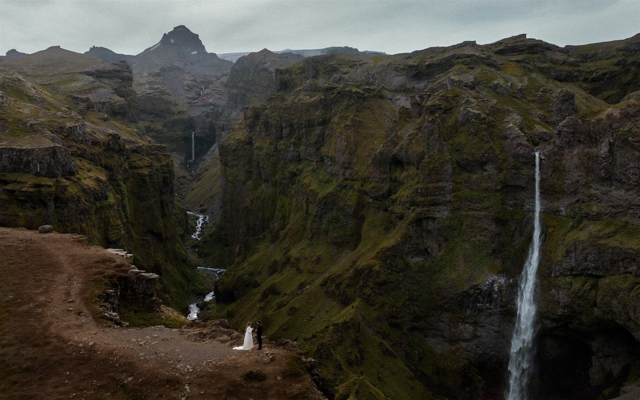 A deep, green valley with multiple waterfalls cascading down steep cliffs under a cloudy sky.