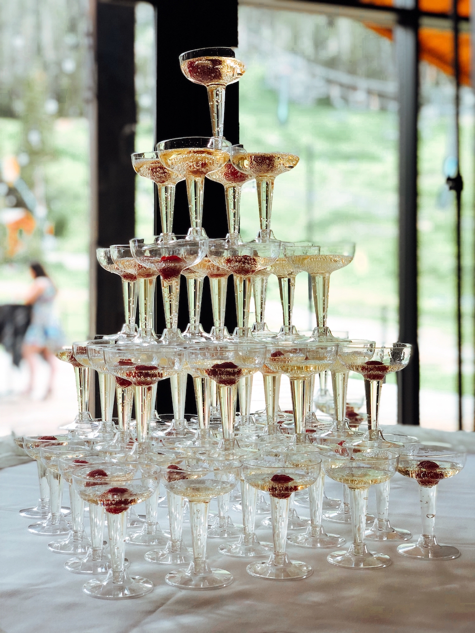 A pyramid of champagne glasses filled with sparkling wine and garnished with red berries, arranged on a white tablecloth.