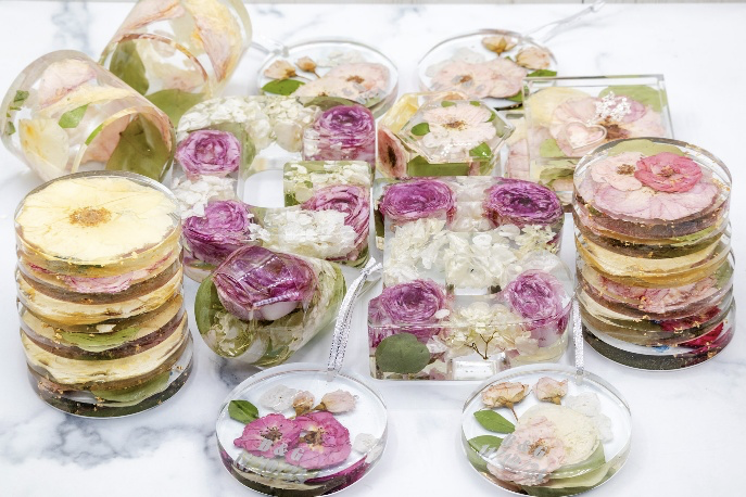 Assorted resin coasters and ornaments with preserved flowers and foliage arranged on a white marble surface.
