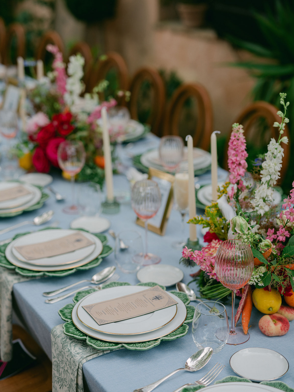 A formal dining table set with plates, glasses, cutlery, candles, and colorful floral centerpieces, featuring a light blue tablecloth.