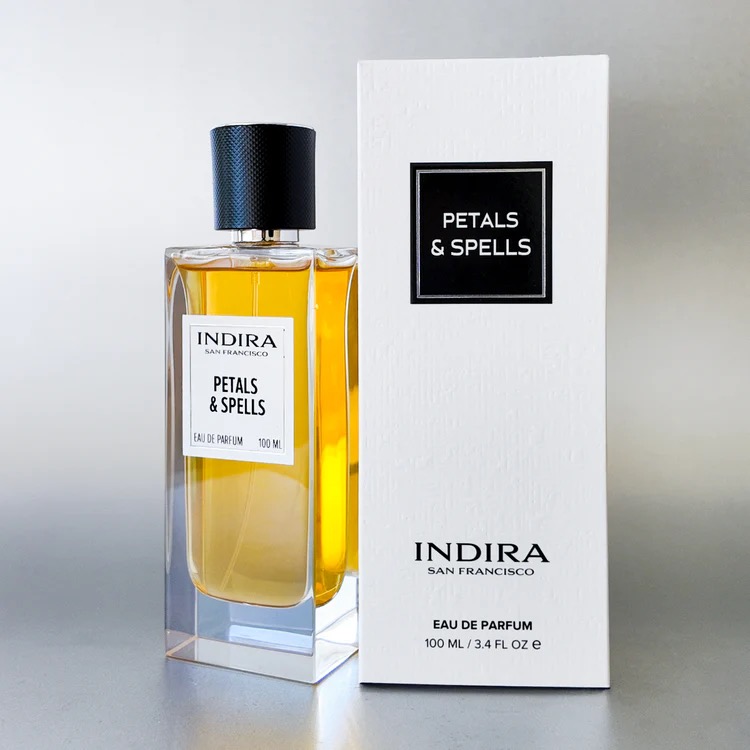 A bottle of Indira Petals &amp; Spells Eau de Parfum stands next to its white box packaging, both labeled with the fragrance name and brand.