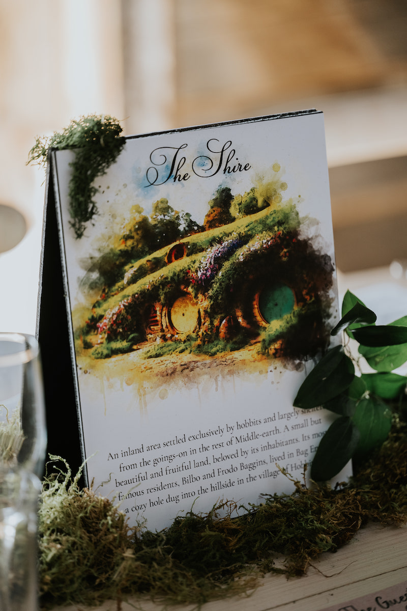 A table card labeled "The Shire" with an illustration of hobbit houses, surrounded by moss and greenery, used as a decorative centerpiece.
