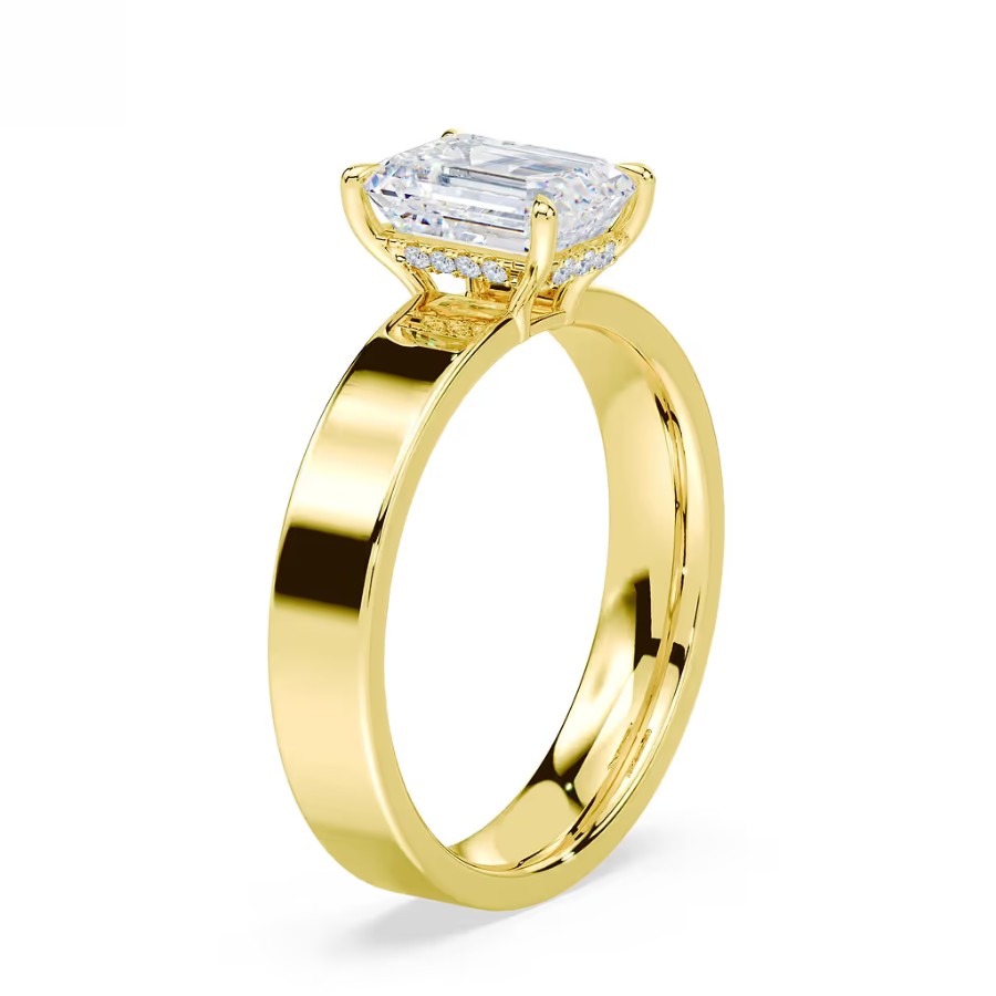A gold ring with a rectangular emerald-cut diamond solitaire set in a raised prong setting.