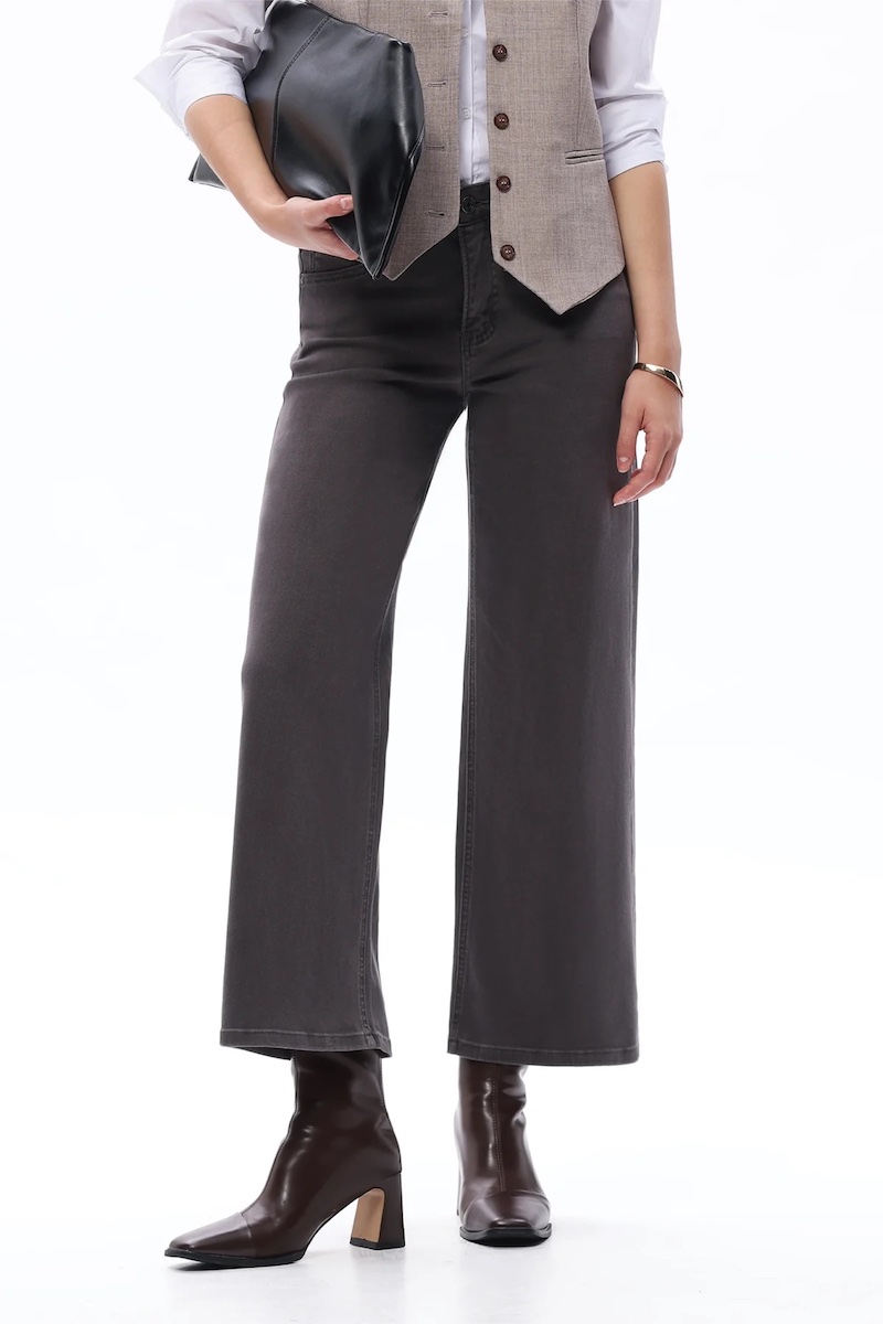 Person wearing dark wide-leg pants, a beige vest over a white shirt, brown ankle boots, and holding a black clutch. The photo is cropped from shoulders down.