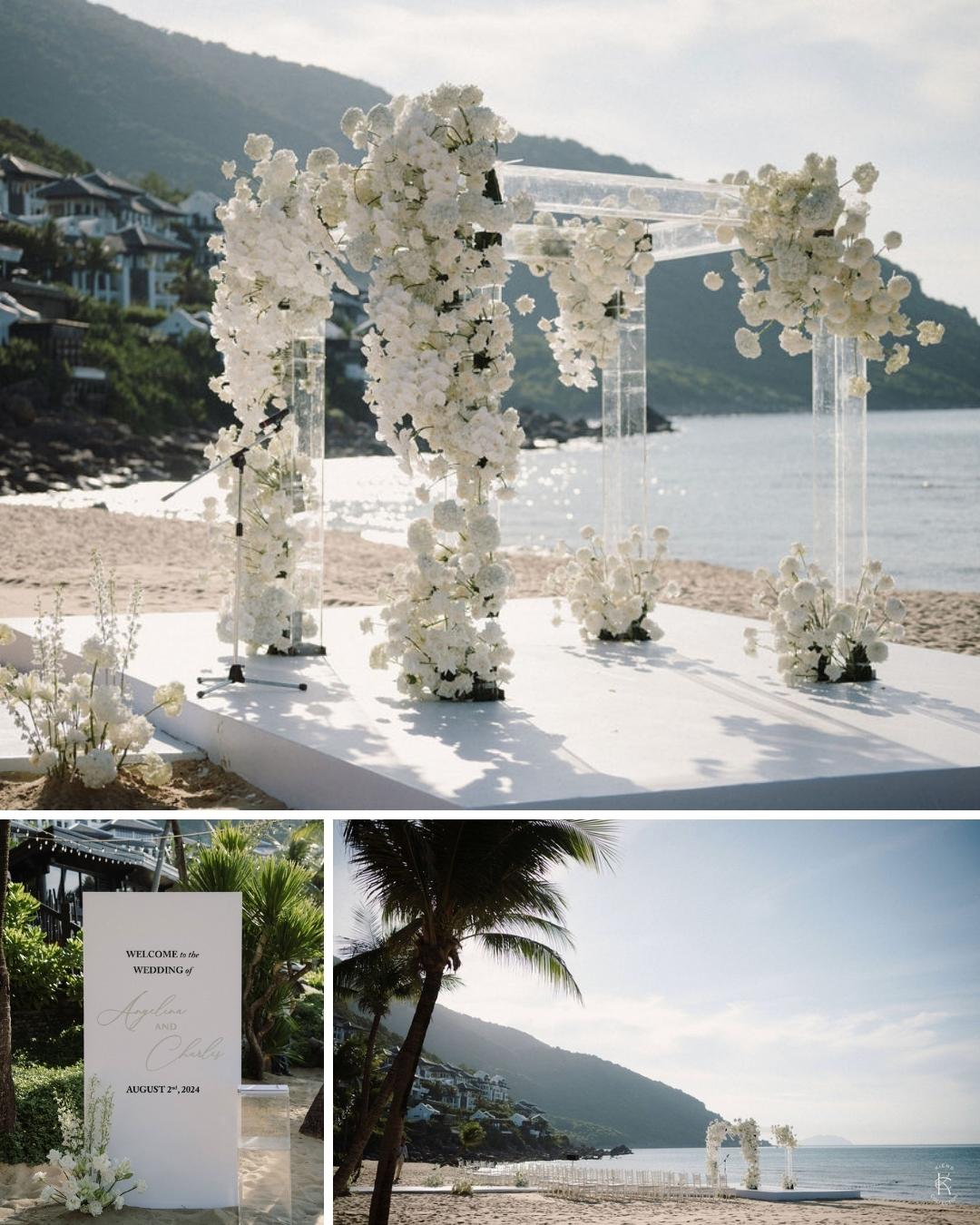 A floral arch decorated with white flowers set up on a beach, with mountains and the ocean in the background; close-up of a wedding sign and palm tree also shown.