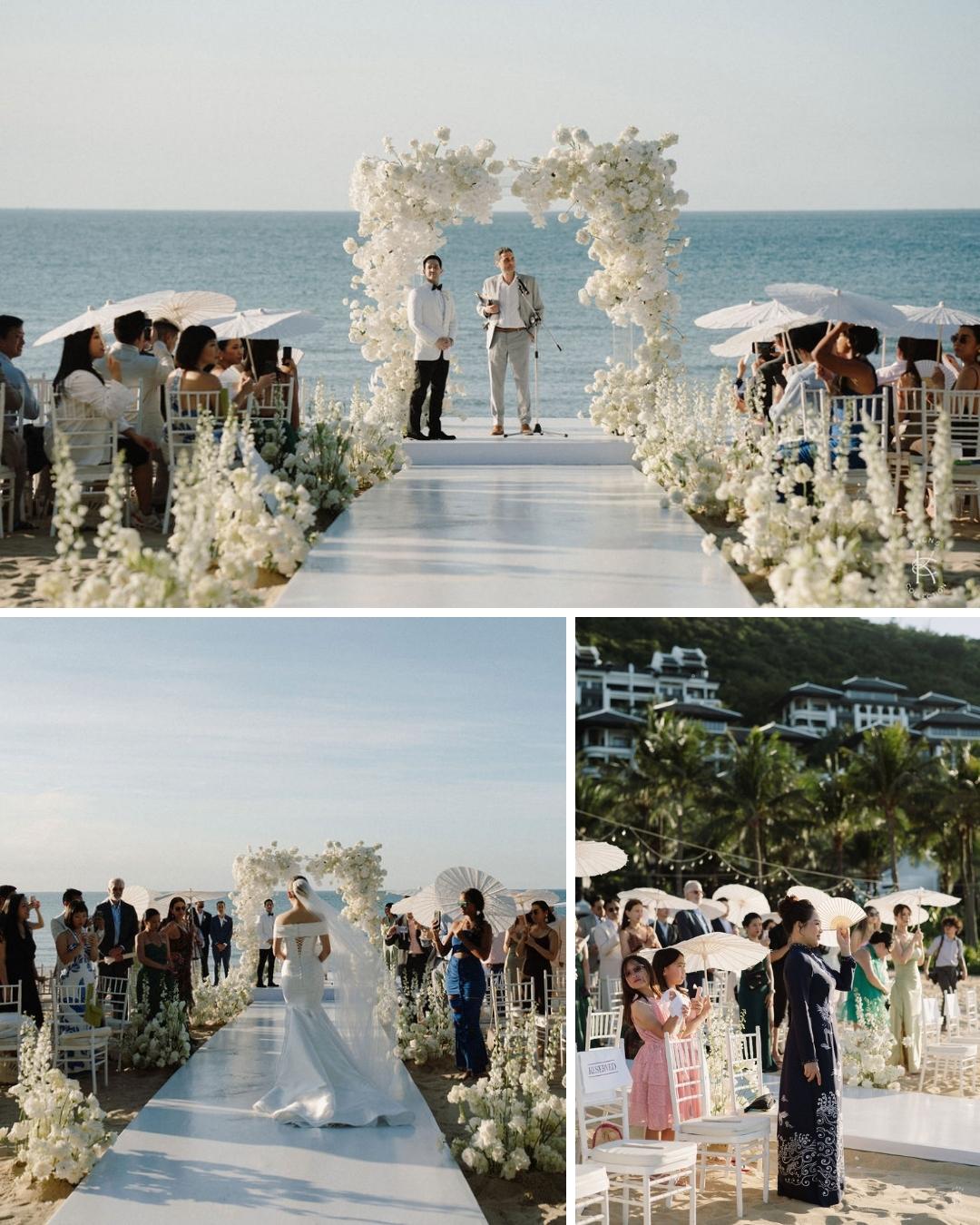 A beachside wedding ceremony with guests seated on either side of a white aisle decorated with white flowers and a floral arch, overlooking the ocean.