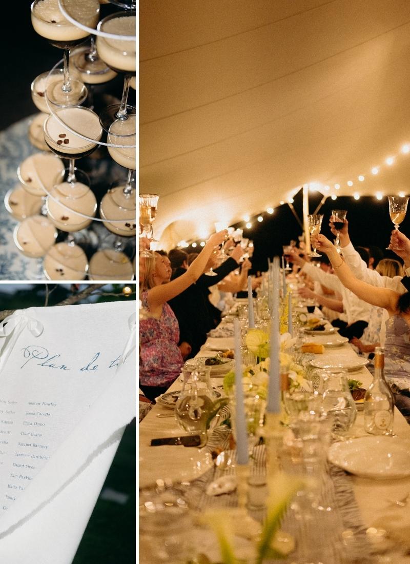 A long dinner table set for an event under string lights, with people raising glasses in a toast and details of cocktails and a printed menu.