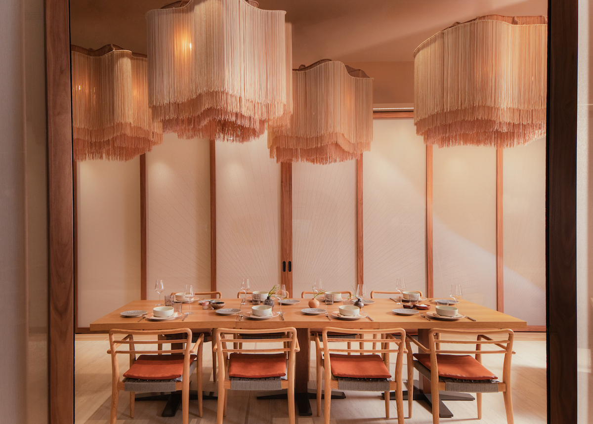 A modern dining room with a wooden table, eight chairs, place settings, and large fringe pendant lights hanging from the ceiling.