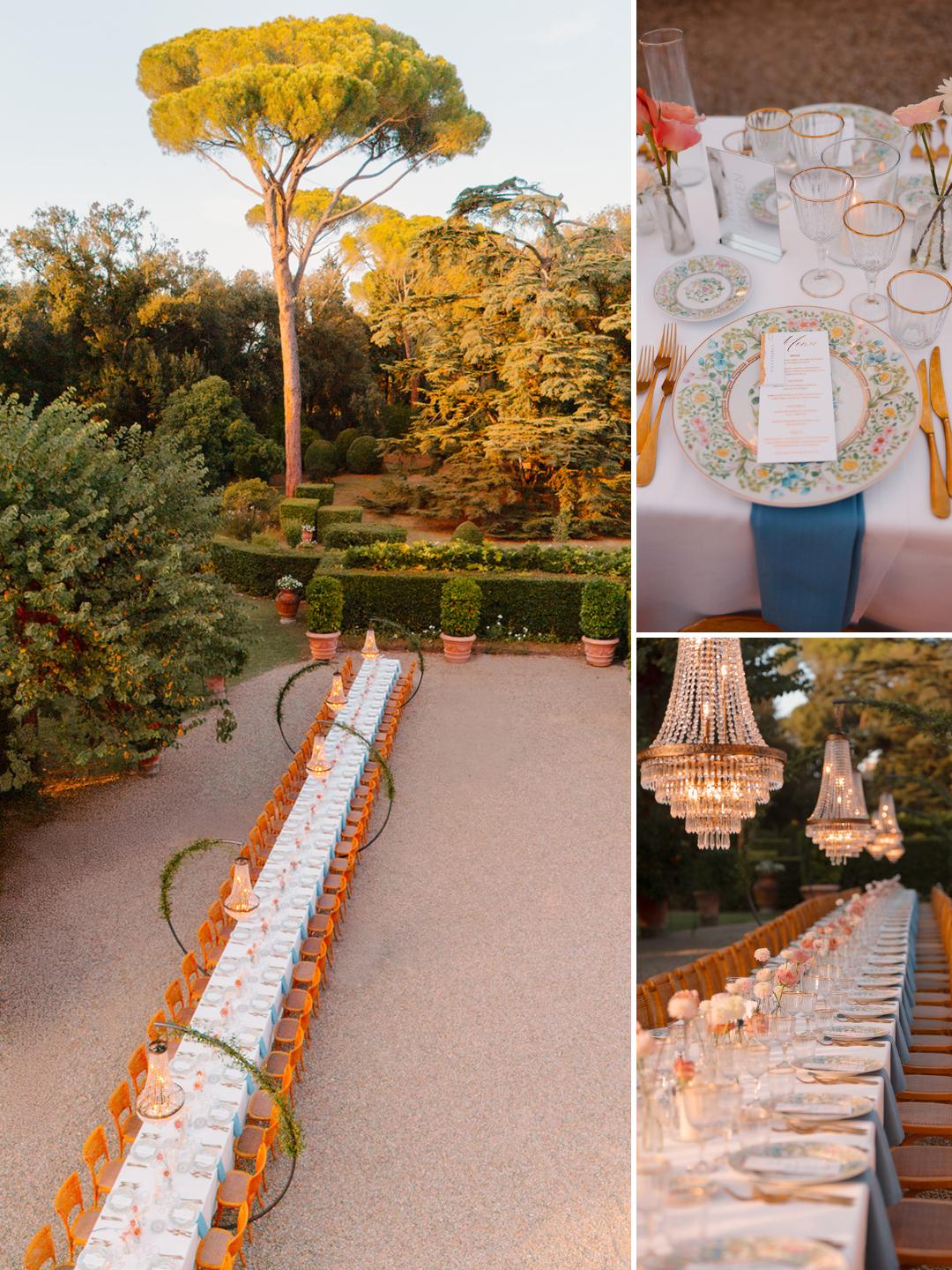 An outdoor garden dining setup with a long table set for many guests, decorated with white linens, gold cutlery, menus, and crystal chandeliers, surrounded by lush greenery.