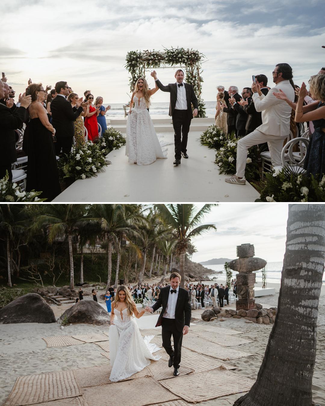 A bride and groom walk together at their outdoor wedding ceremony, surrounded by guests and tropical scenery.