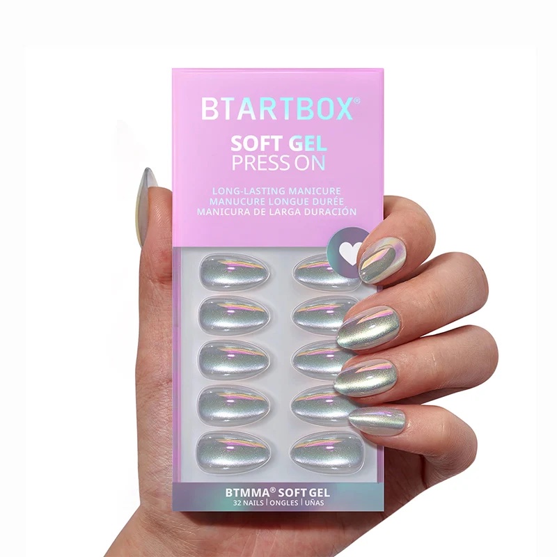 A hand holds a box of BTArtbox Soft Gel Press On nails, featuring shiny, light chrome-colored press-on nails displayed in the packaging.
