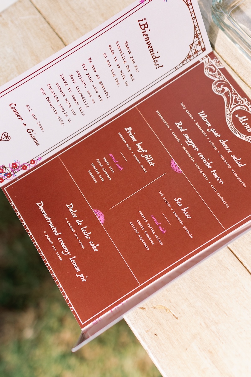 A close-up of an open restaurant menu with brown and cream pages, displayed on a wooden table. Text and food offerings are visible but not fully readable.