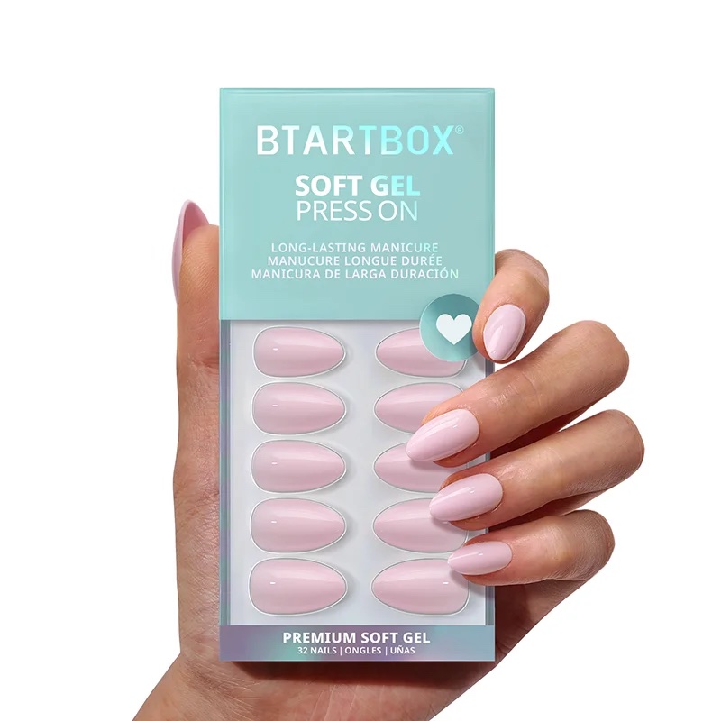 A hand holds a box of BTArtBox soft gel press-on nails in a light pink color, with matching nails applied on the fingers.
