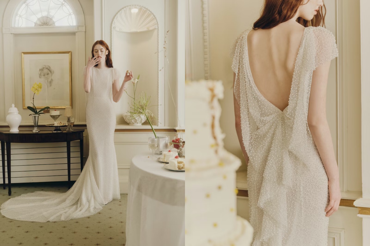 A woman in a white, floor-length wedding dress with a low back stands in an elegantly decorated room near a table with a cake.