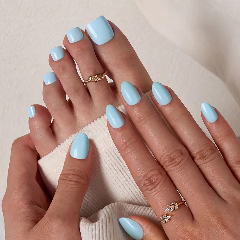 Close-up of hands and feet with light blue nail polish, gold rings on one finger and two toes, and a white fabric partially covering the hand.