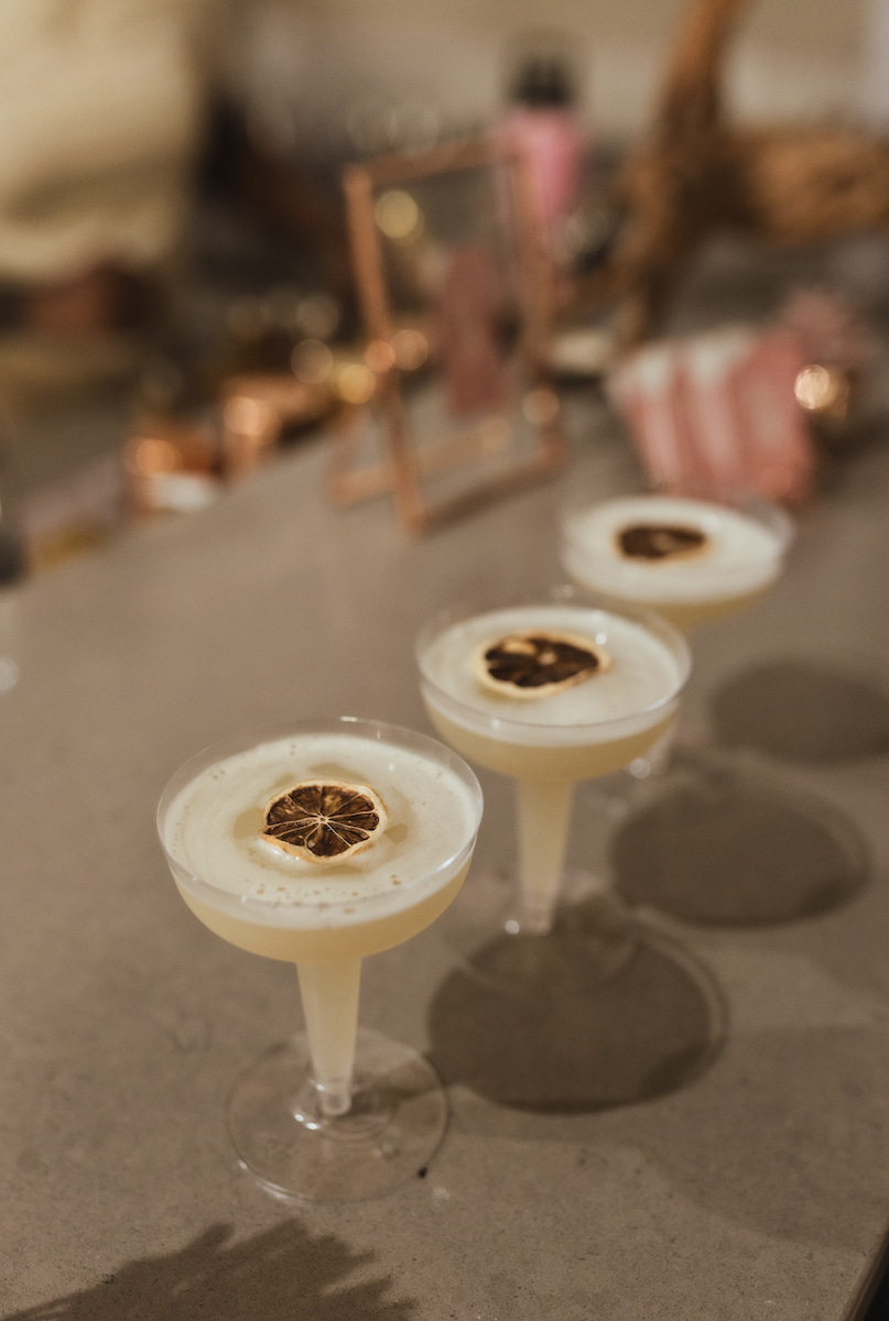 Three coupe glasses filled with a creamy cocktail, each garnished with a toasted slice, are arranged in a row on a countertop.