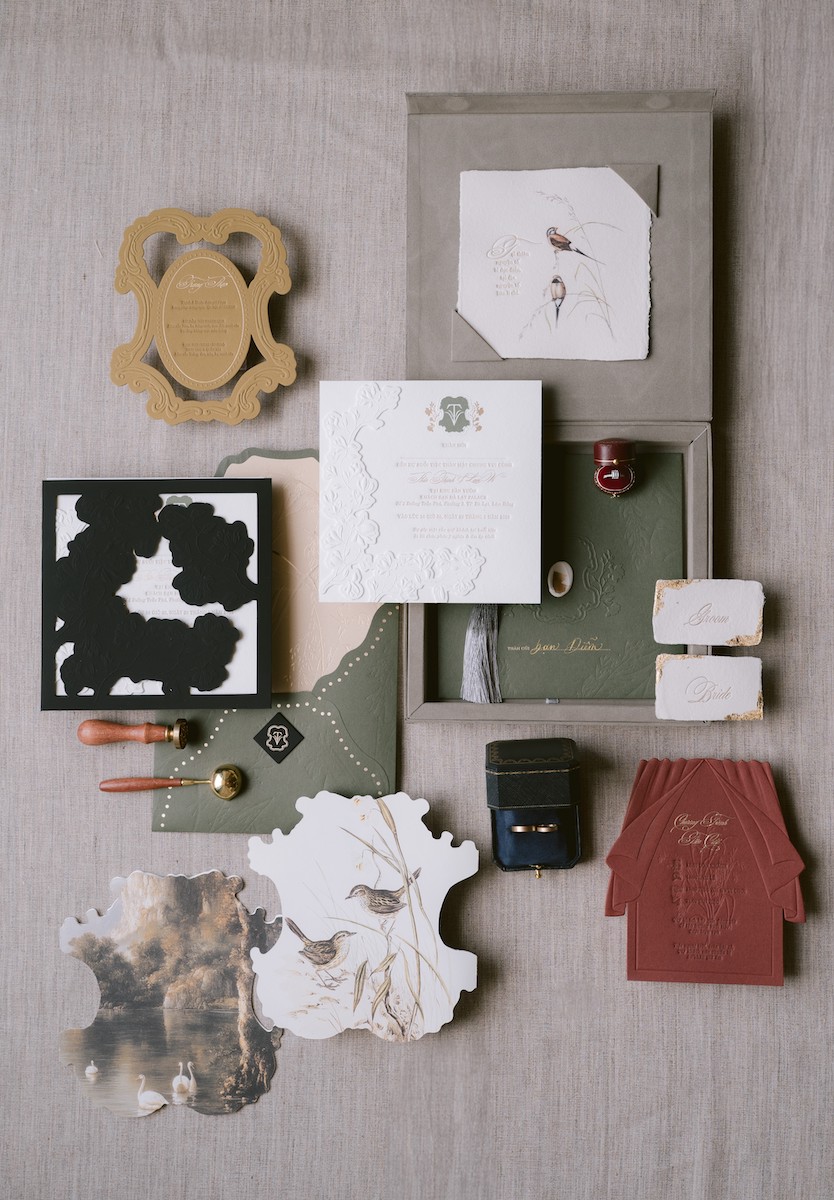 Flat lay of assorted stationery items including cards, envelopes, paper samples, a wax seal, and a small box arranged on a beige fabric surface.