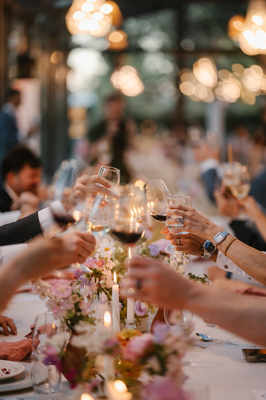 People raising wine glasses in a toast at a long, decorated table during an event or celebration.