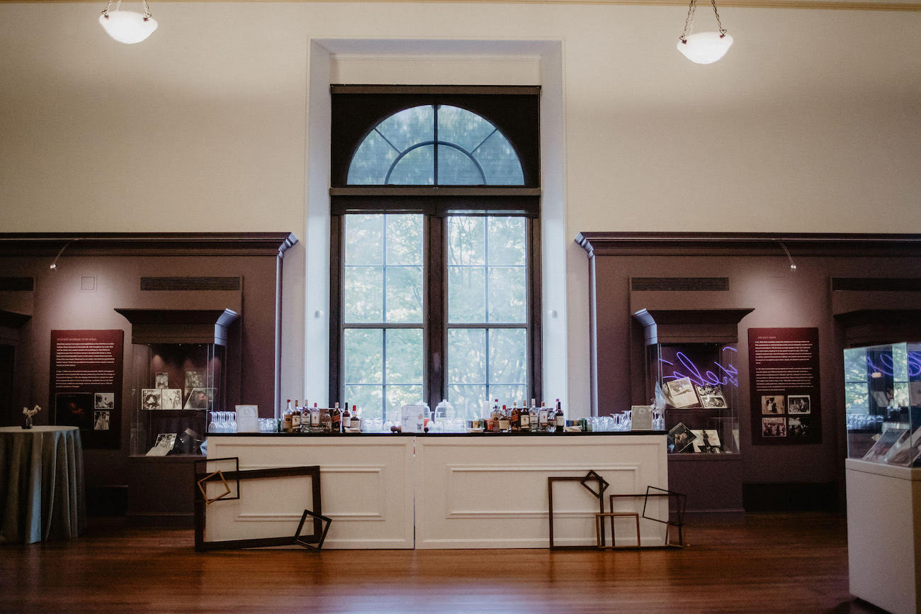 A museum exhibit room with a large central window, display cases, informational panels, and various artifacts arranged on counters and stands.