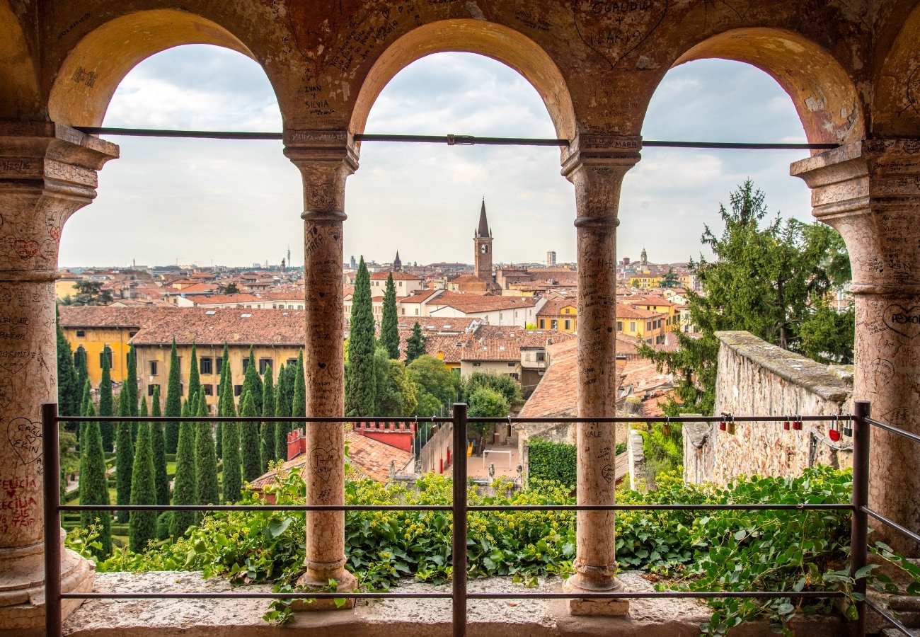 View of a cityscape with red rooftops, trees, and a distant church spire, seen through three arched stone columns.