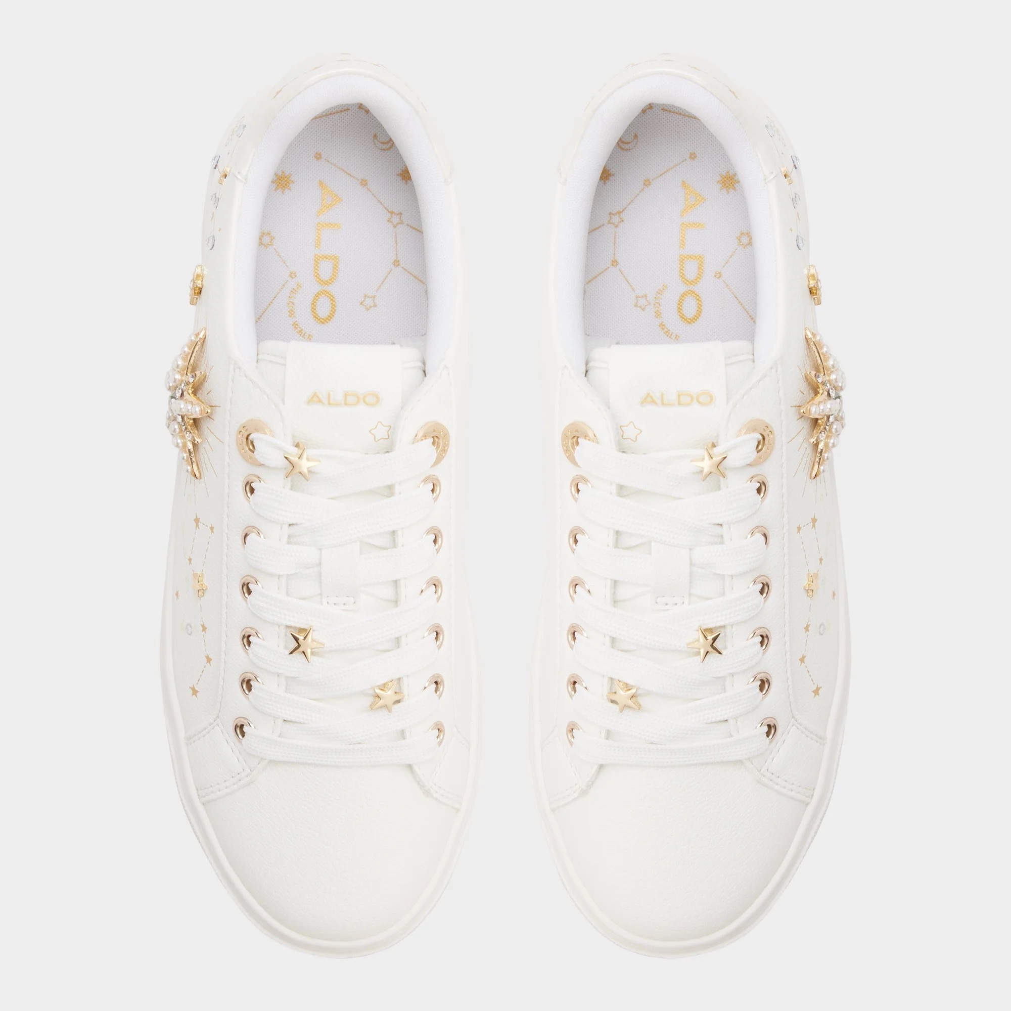 Top view of a pair of white ALDO sneakers with gold accents, gold eyelets, and decorative gold embellishments on the sides.