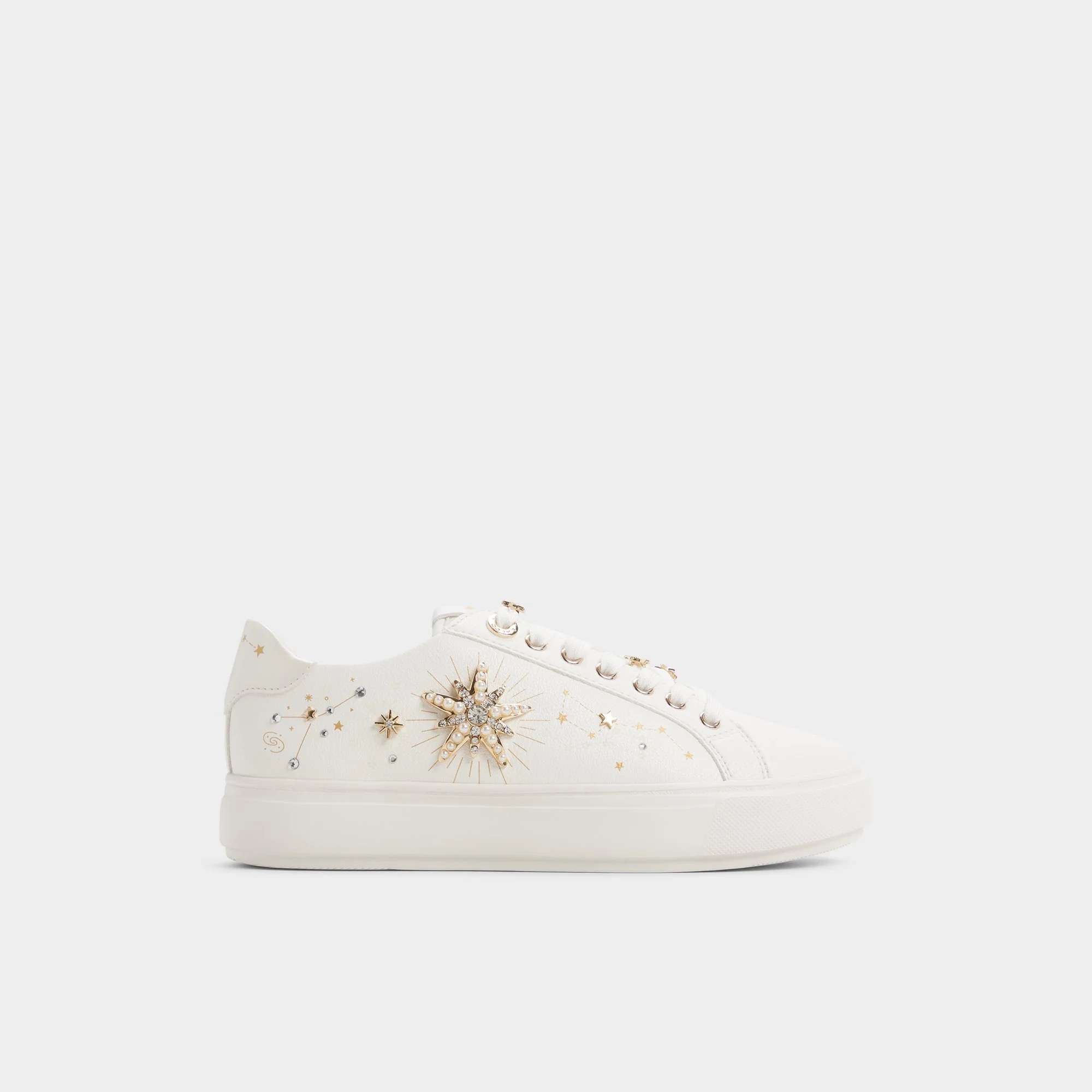 White low-top sneaker with gold star and sun embellishments on the side, gold eyelets, and a plain white sole against a plain background.