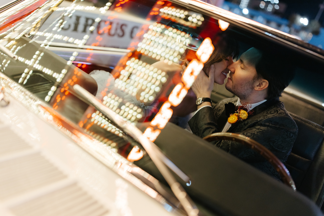 A couple sits in a car at night, kissing and smiling, with neon lights and the word "Circus" reflected on the windshield.