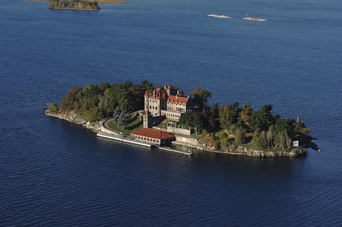 A small island in a body of water features a large, historic-looking building surrounded by trees and a dock along the shore.