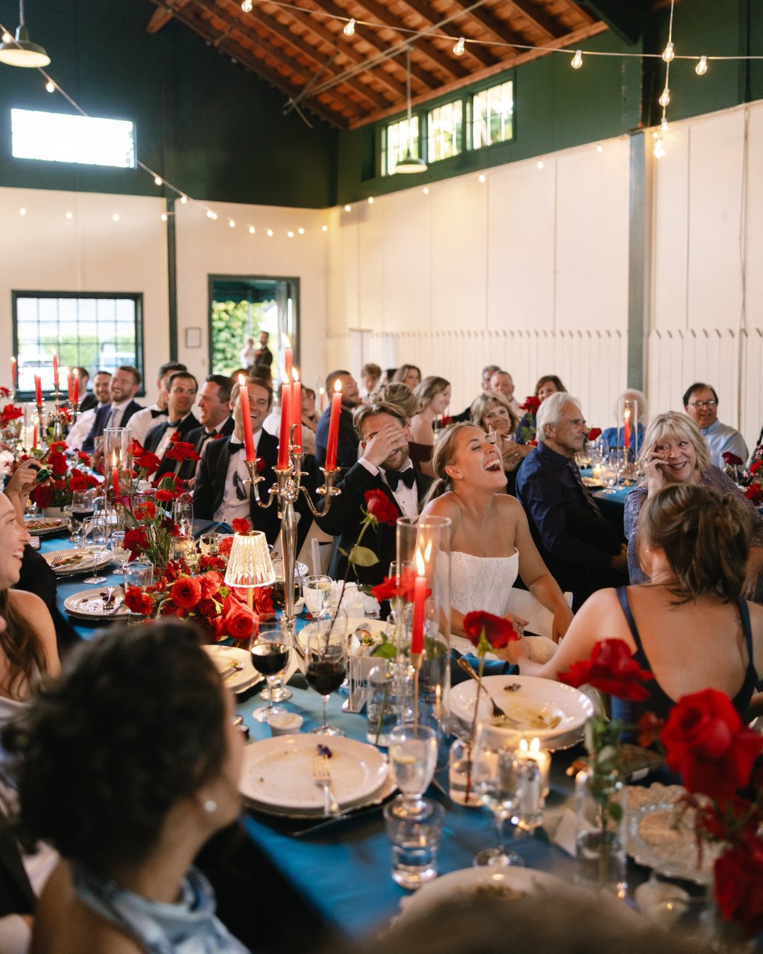 A large group of people sit at a long, decorated table indoors, appearing to celebrate an event, possibly a wedding reception.